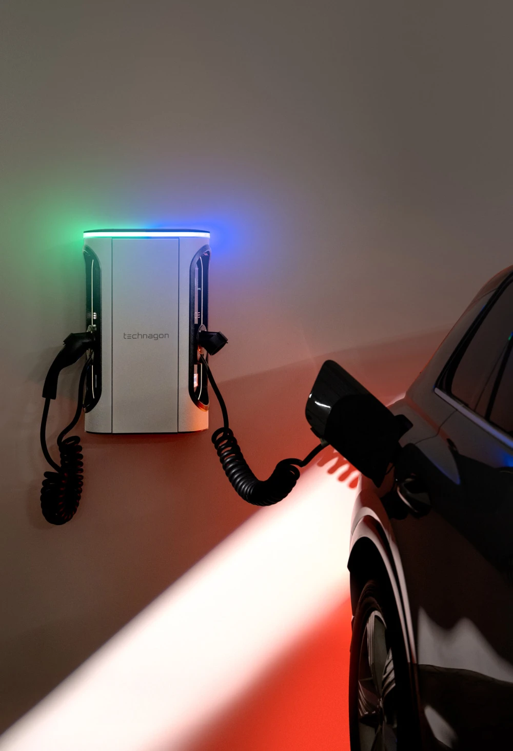 Technagon TEW4 an einer Wand mit zwei Ladepunkten, Spiralkabeln und leuchtender Lichtleiste; an einem Ladepunkt lädt ein Auto