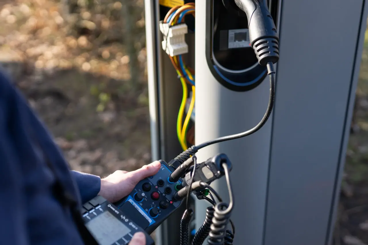 Elektrofachkraft misst mit einem Prüfgerät an einer geöffneten Technagon-Ladesäule