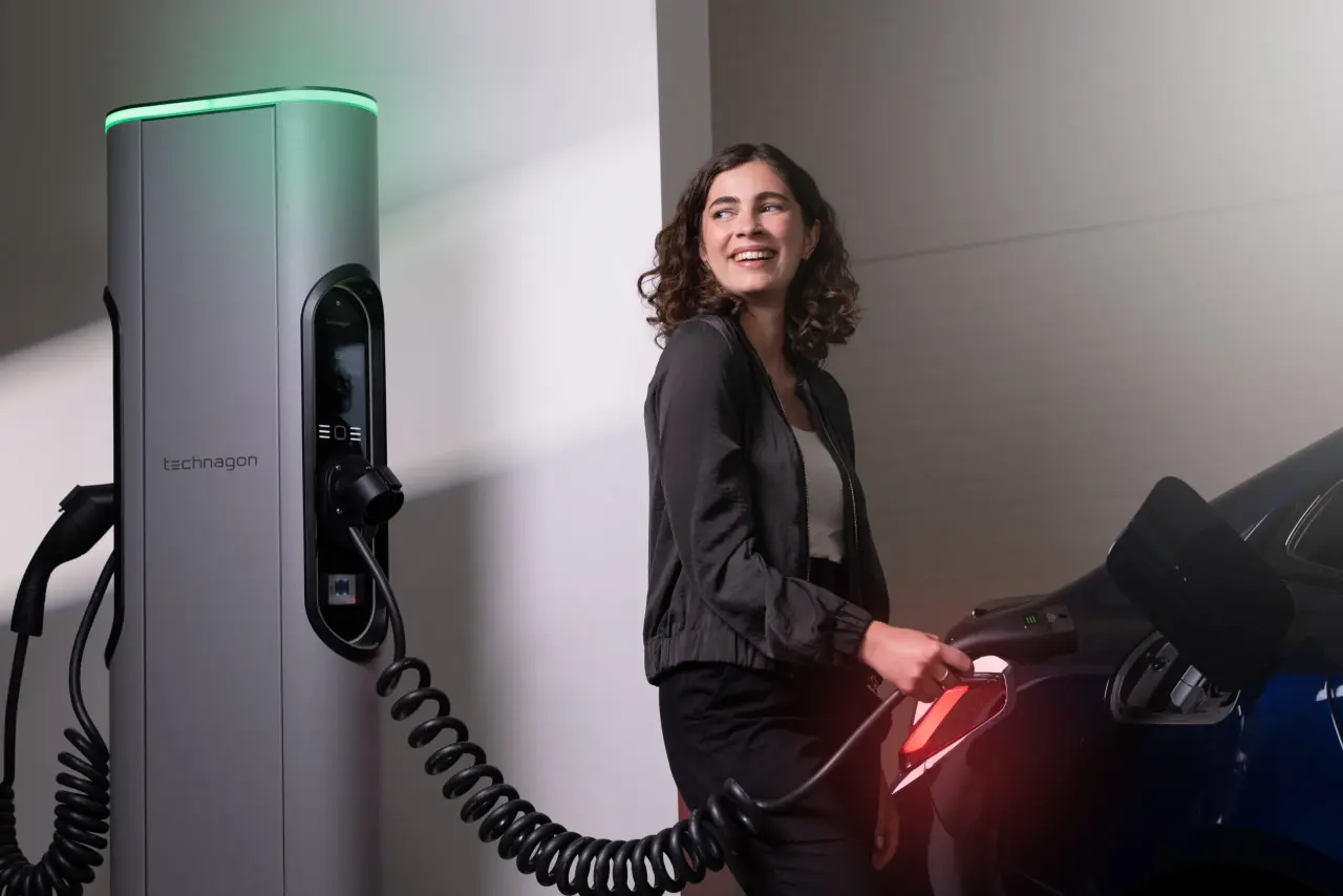 Technagon TEP4 mit grüner Lichtleiste und Spiralkabel; eine Frau steckt den Ladestecker in ein Elektroauto