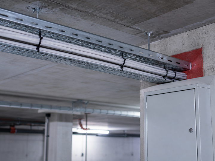 Kabeltrasse unter der Decke einer Tiefgarage, die zu einem Verteilerschrank führt